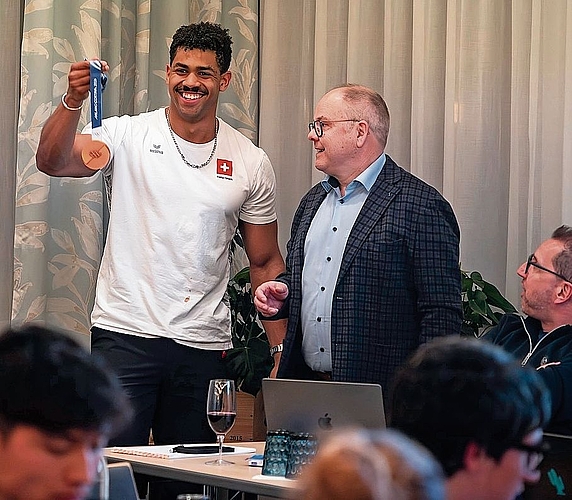 Präsident Felix Muff gratuliert Amadou Ndiaye, der mit Freude seine Olympia-Bronzemedaille aus dem Bobwettbewerbe zeigt.