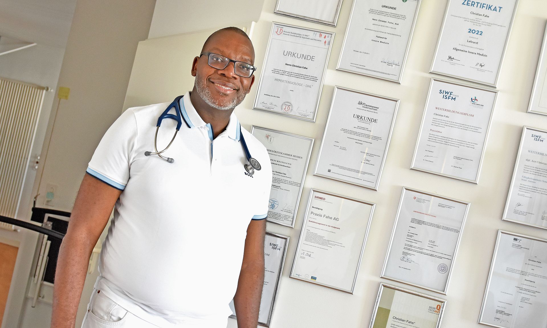 Christian Fahe vor seinen Diplomen und Weiterbildungsnachweisen. Der Facharzt für Allgemeine Innere Medizin und Nephrologie verfügt über zahlreiche Zusatzqualifikationen in verschiedenen medizinischen Fachbereichen.